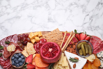 Wooden plate with different delicious snacks on white marble table, top view. Space for text