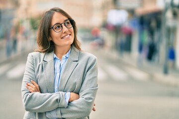 Young hispanic businesswoman with arms crossed smiling happy at the city