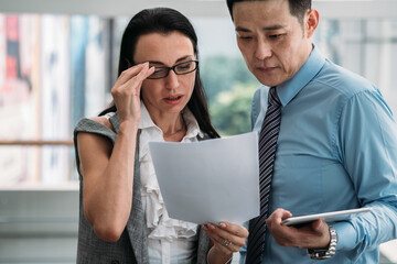 Worried businesswoman and businessman reading documents together.
Two business colleagues standing and reading new information about business project on paper and tablet