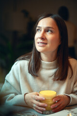 Young caucasian woman smiling and holding a glass of hot turmeric milk on table