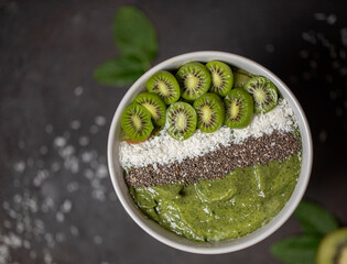 Close up of green healthy fresh spinach kiwi smoothy in bowl with berry kiwi topping with chia seeds and coconut flakes. Detox dieting, clean eating, vegan food concept. Top view with copy space. 