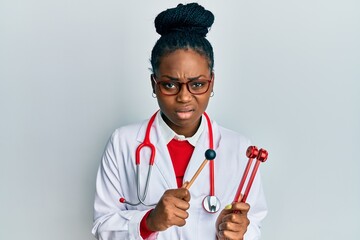Young african american woman wearing doctor uniform holding tuning fork clueless and confused...