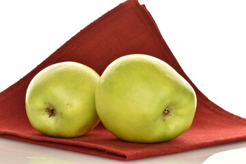 Two sweet green apples by Renet Simirenko on a red linen napkin, close-up, isolated on white.