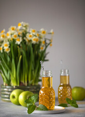 Close up of fresh apple juice in bottles on table with green apples mint and bouquet of daffodils. Fresh healthy drink. High quality photo