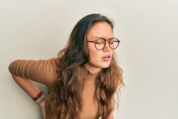 Young hispanic girl wearing casual clothes and glasses suffering of backache, touching back with hand, muscular pain