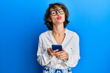 Young brunette woman using smartphone looking at the camera blowing a kiss being lovely and sexy. love expression.