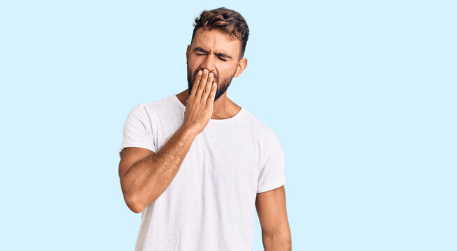 Young hispanic man wearing casual white tshirt bored yawning tired covering mouth with hand. restless and sleepiness.