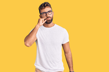 Young hispanic man wearing casual clothes and glasses mouth and lips shut as zip with fingers....