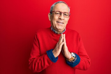 Handsome senior man with grey hair wearing casual clothes and glasses praying with hands together asking for forgiveness smiling confident.