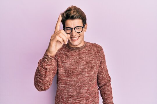 Handsome caucasian man wearing casual sweater and glasses pointing finger up with successful idea. exited and happy. number one.