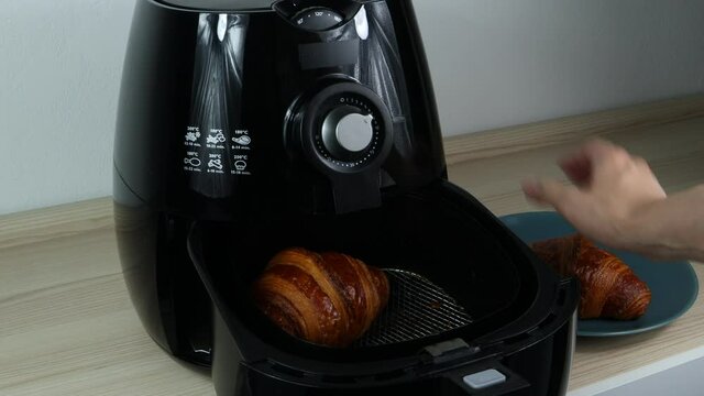 homemade croissant is taken out of the black air fryer or oil free fryer appliance on the wooden table with background of white cement wall in the kitchen for being breakfast in the moring