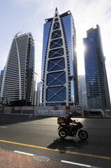 Vue sur une route et des buildings à Dubaï. Une motocyclette au premier plan, les gratte-ciel au second, et le soleil descendant formant un joli contre-jour en clair-obscur.