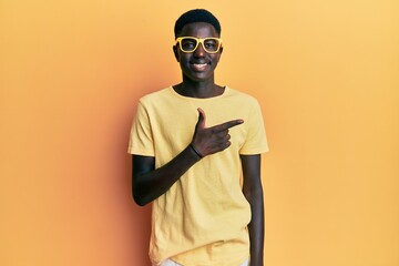 Young african american man wearing casual clothes and glasses cheerful with a smile of face pointing with hand and finger up to the side with happy and natural expression on face