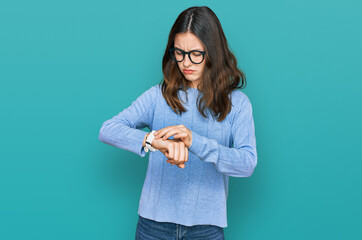 Young beautiful woman wearing casual clothes and glasses checking the time on wrist watch, relaxed...