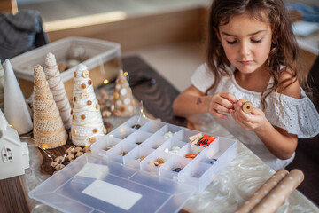 Cute little girl with curly hair making crafts and decorating Christmas Tree cone with buttons.