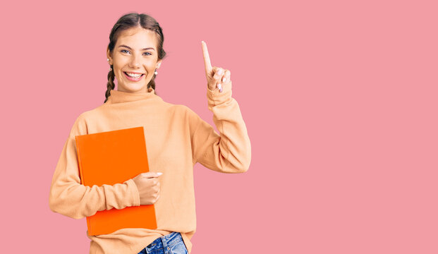 Beautiful caucasian woman with blonde hair holding book surprised with an idea or question pointing finger with happy face, number one