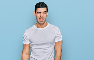 Obraz premium Handsome hispanic man wearing casual white t shirt winking looking at the camera with sexy expression, cheerful and happy face.