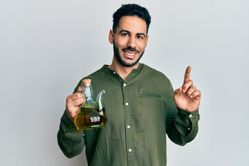 Young hispanic man holding olive oil can smiling with an idea or question pointing finger with...