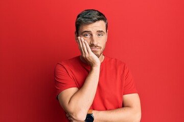 Handsome caucasian man wearing casual red tshirt thinking looking tired and bored with depression problems with crossed arms.