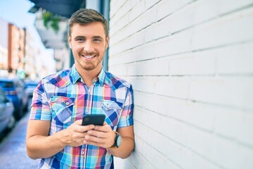 Obraz premium Young caucasian man smiling happy using smartphone at the city.