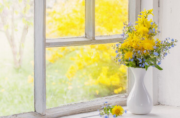 dandelions and forget-me-not in vase on windowsill