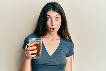 Young caucasian woman holding cup of tea scared and amazed with open mouth for surprise, disbelief...