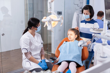 Dentist wearing face mask in the course kid examination with dental bib in dentistiry office....
