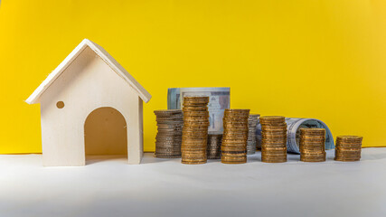 House, stacked coins and paper money on white table with yellow background