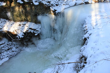 eiszeit im winter mit schnee in der landschaft und im wald eingeforener wasserfall mit eiszapfen...