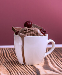 pudding with ice cream, cherries and pieces of chocolate in a mug on a jjon wood table. Melted ice cream flows in a mug on a pink background. High quality photo