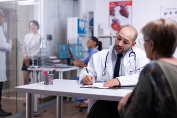 Specialist doctor prescribing treatment for senior woman writting on clipboard. Older patient visiting physician telling about health complaints, medical practitioner asking questions talking about