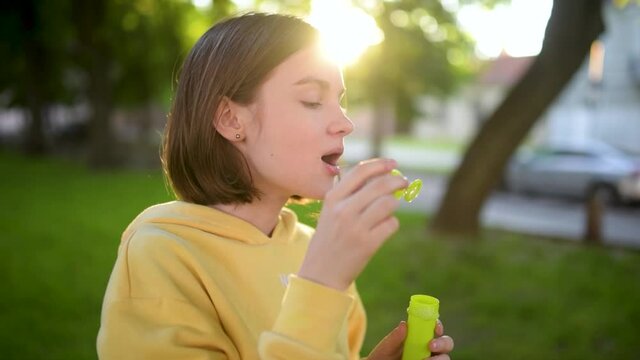 Pretty teenage girl blowing soap bubbles on a sunset. Child having fun in a park in summer. Funny activities for kids.