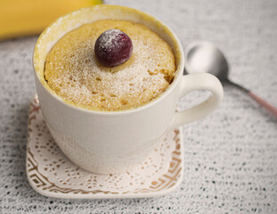 banana cupcake in a mug. Muffin banana cooked in the microwave. Decorated with a cherry. White mug with dessert and fresh banana in the background. High quality photo