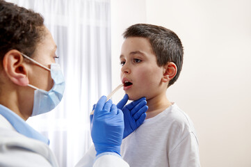 Young pediatrician examining little boys throat to diagnose his illness.