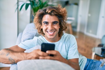 Young hispanic man smiling happy using smartphone at home