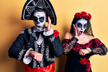 Young couple wearing mexican day of the dead costume over yellow looking at the watch time worried, afraid of getting late