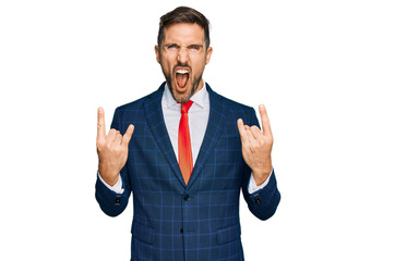Handsome man with beard wearing business suit and tie shouting with crazy expression doing rock symbol with hands up. music star. heavy concept.