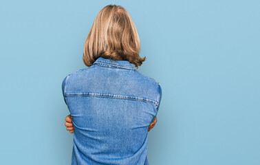 Caucasian man with blond long hair wearing casual denim jacket standing backwards looking away with...