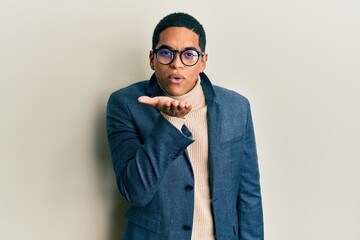Young handsome hispanic man wearing elegant clothes and glasses looking at the camera blowing a...