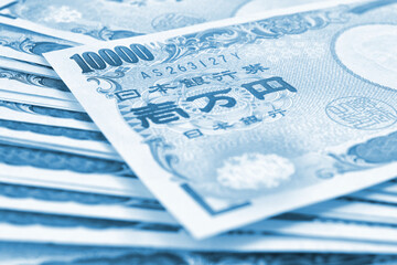 Obraz premium Light background on the theme of Japanese money, finance and economy. Blue tinted backdrop. Yen banknotes close-up. Blurred with focus on 10,000. View from above. Macro