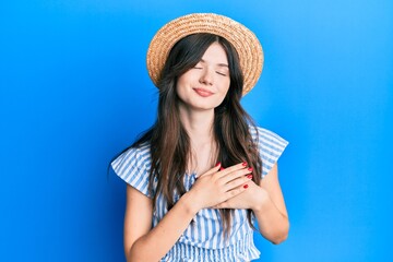 Young beautiful caucasian girl wearing summer hat smiling with hands on chest, eyes closed with grateful gesture on face. health concept.