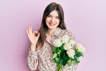 Young beautiful caucasian girl holding bouquet of white flowers doing ok sign with fingers, smiling friendly gesturing excellent symbol