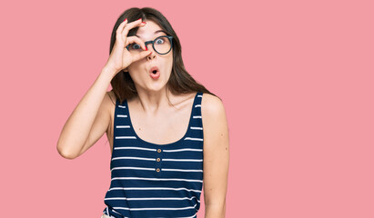 Young beautiful caucasian girl wearing casual clothes and glasses doing ok gesture shocked with surprised face, eye looking through fingers. unbelieving expression.