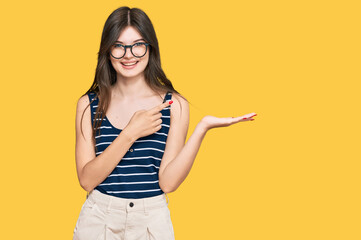 Young beautiful caucasian girl wearing casual clothes and glasses amazed and smiling to the camera while presenting with hand and pointing with finger.