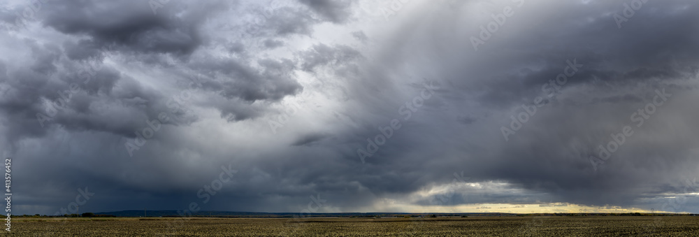 Wall mural dramatic blue-gray storm clouds over a very wide panoramic prairie landscape with a gravel road exte