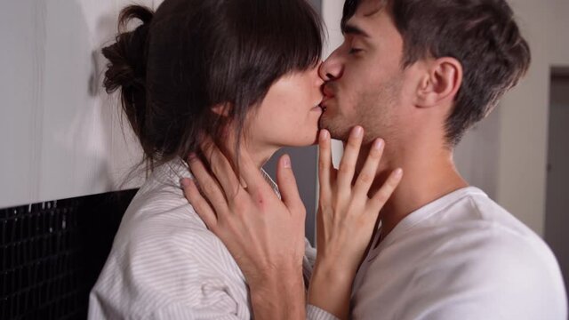 Close-up of caucasian couple kissing passionately at home in the morning. Love relationship between a man and a woman. A brunette in a man's light shirt.