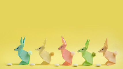 Paper Easter bunnies-origami made of colored paper on a delicate yellow background. The concept of the celebration of Easter, greeting card, crafts with your own hands.