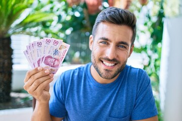 Young hispanic man smiling happy holding mexican pesos banknotes at the terrace.