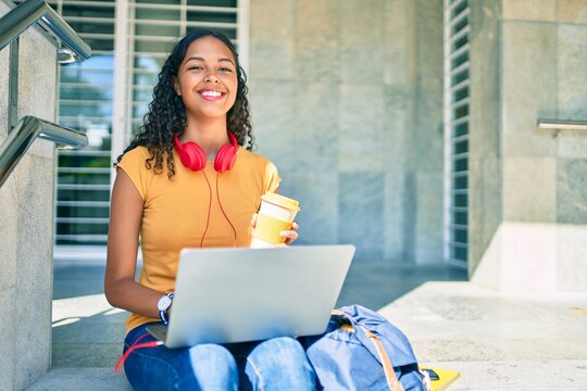 Young african american student girl using laptop sitting on stairs at university.