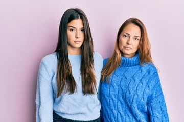 Hispanic family of mother and daughter wearing wool winter sweater relaxed with serious expression on face. simple and natural looking at the camera.